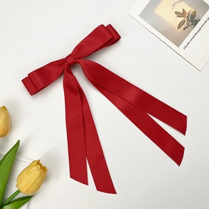 Elegant deep red satin bow hair clip with long ribbons on white background with tulips