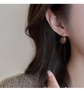 Close-up of a model wearing brown teardrop beads on gold geometric hoop earrings