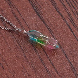 Detailed close-up of rainbow crystal pillar pendant wrapped in silver wire on wood