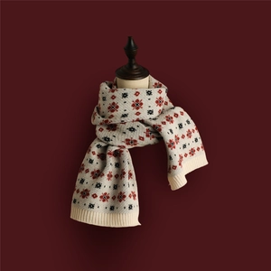 Close-up of beige knitted Christmas scarf with red festive patterns on a red background