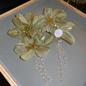 Detail view of green fabric flower earrings with crystal tassels on a velvet tray