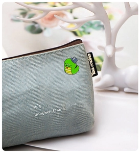 Detail of cute snake enamel pin on light blue denim bag with branded logo side label