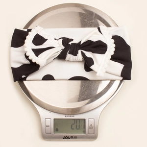 Detailed view of cow print baby headband weighing 20.1g with white pom pom lace edges