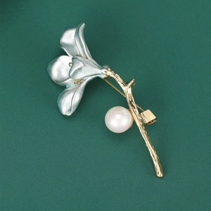 Macro shot of silver lily flower brooch with golden stem and elegant white pearl detail
