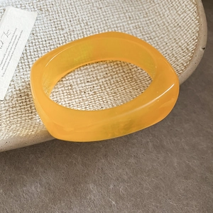 Close-up of geometric orange resin bangle resting on a textured beige dish in retro style