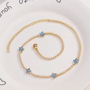 Detail of gold flower bracelet with blue stones and clear zircon on a white plate
