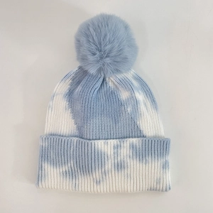 Detail view of tie-dye knit beanie with large faux fur pompom and ribbed texture