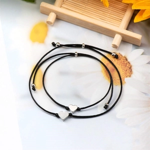 Détail de bracelets faits main en cordon noir avec breloques cœur argentées sur carte fleurie