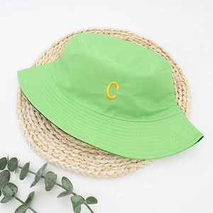 Close-up of bright green bucket hat with yellow C embroidery on woven straw mat