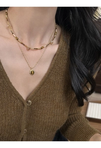 Close-up of double-layer gold necklace with oval tiger eye pendant on a female model