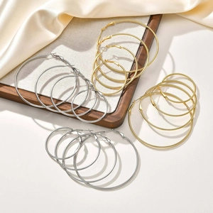 Set of large stainless steel hoop earrings in gold and silver finish on a wooden tray