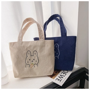 Detail of embroidered cartoon rabbit holding a carrot on white corduroy tote bag