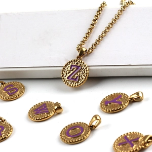 Detailed shot of golden alphabet pendants with purple enamel inlay and textured edges