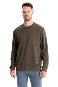 Close-up of olive green crewneck sweatshirt showing ribbed hem and fashion textile label