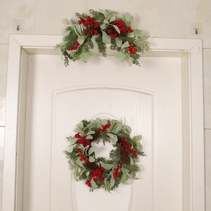 Christmas wreath and door swag set with red berries, green leaves and pine cones on white door