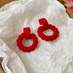 Detail of red twisted hoop earrings with a matte texture on white crinkle paper