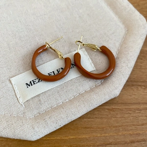 Close-up of caramel resin C-shaped hoop earrings on a canvas pouch and wooden table