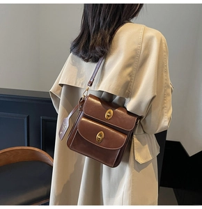 Detail of vintage brown leather crossbody bag with dual gold twist locks on khaki trench coat