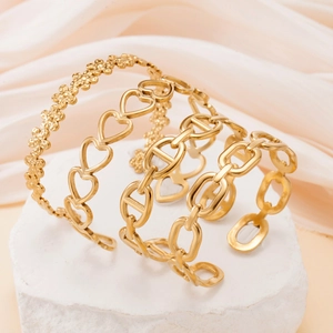 Dettaglio di tre bracciali rigidi dorati in acciaio inossidabile con fiori e cuori