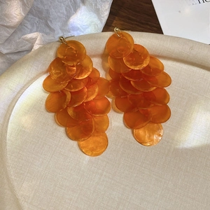 Detail of long orange shell tassel earrings with layered round resin discs on a beige tray