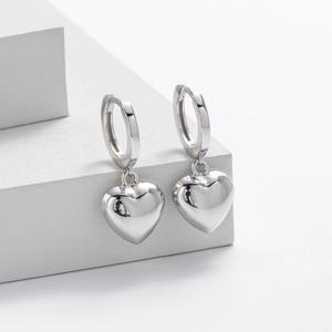 Detailed view of polished sterling silver heart dangle earrings on a geometric stand