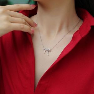 Detail of S925 silver bow necklace with tassels on a model wearing a red shirt