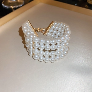 Detail of four-layer white pearl necklace with gold metal clasp on beige tray