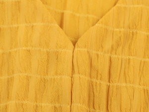 Dettaglio del vestito giallo con scollo a V caratterizzato da texture seersucker e pieghe