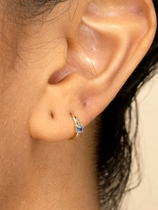 Primer plano de aro de oro de 18k con circón azul oscuro engastado en la oreja