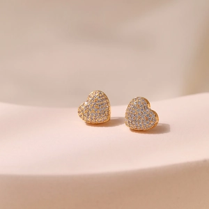Macro shot of gold heart stud earrings with white cubic zirconia pavé setting on a stand