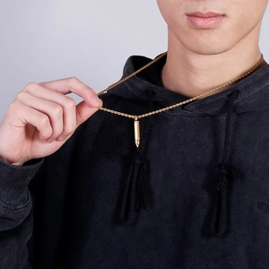 Detailed view of a gold bullet pendant necklace with a twisted chain on a male model