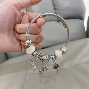 Silver bead bracelet with clover charm and heart key pendant held against a grey sofa