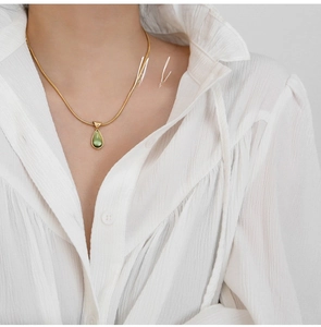 Close-up of gold snake chain necklace featuring a pear-shaped olive green pendant