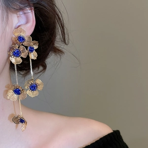 Close-up of golden hollow flower tassel earrings with blue gemstones worn by a model