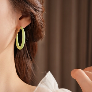 Close-up of light green matte circular hoop earrings with gold clasp worn by a model