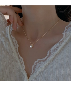 Close-up of a single white pearl pendant on a delicate gold chain on a woman's collarbone