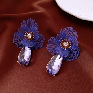 Détail de boucles d'oreilles fleur dorées avec cristaux violets sur tissu brun