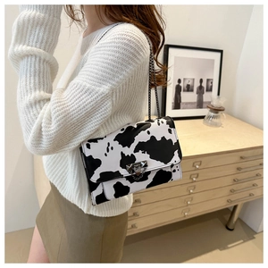 Detail of cow print crossbody bag featuring a metal chain strap and sleek metallic lock