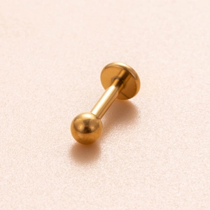 Polished golden G23 titanium labret stud with flat base and round bead on pink surface