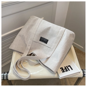 Detail of cream canvas tote bag with black label on a modern chair with a book