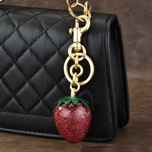 Sparkling red strawberry bag charm with gold hardware on a quilted handbag