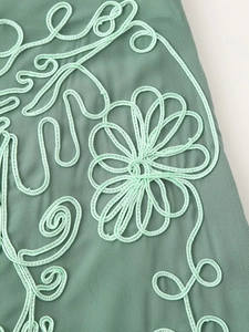 Macro d'une broderie florale vert clair détaillée sur un tissu de style complexe