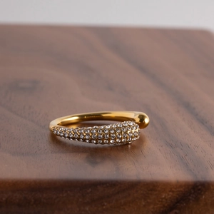 Close-up of golden open ring with pavé-set diamonds on a wooden surface