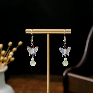 Detail of butterfly drop earrings with colorful charms and red beads on gold stand