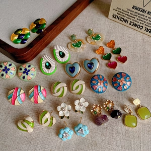 Flat lay of colorful enamel heart and floral stud earrings on a rustic linen background