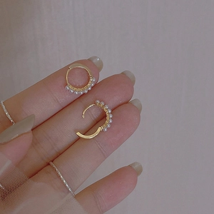 Minimalist gold hoop earrings with small white pearls held between fingers for size
