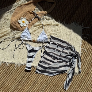 Detailed flat lay of a striped three-piece bikini set with a matching mesh sarong wrap