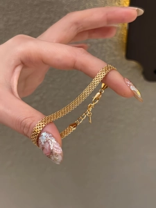 Dettaglio di un bracciale a catena in maglia dorata a tre strati con chiusura a moschettone