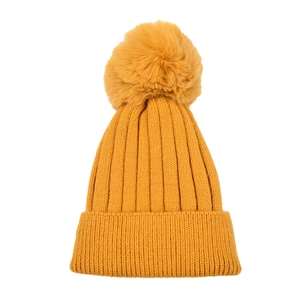 Detail of mustard yellow knit beanie showing ribbed texture and large faux fur pompom