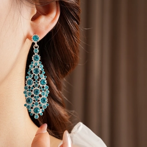 Detalle de pendientes colgantes geométricos plateados con circonitas azules en modelo